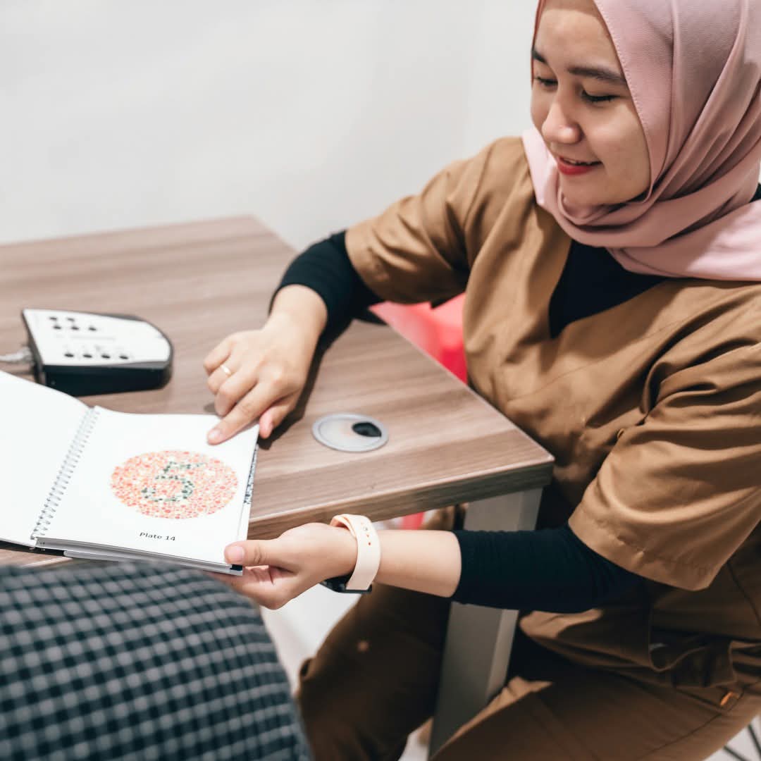 A health worker wearing a hijab showing a client a vision assessment booklet