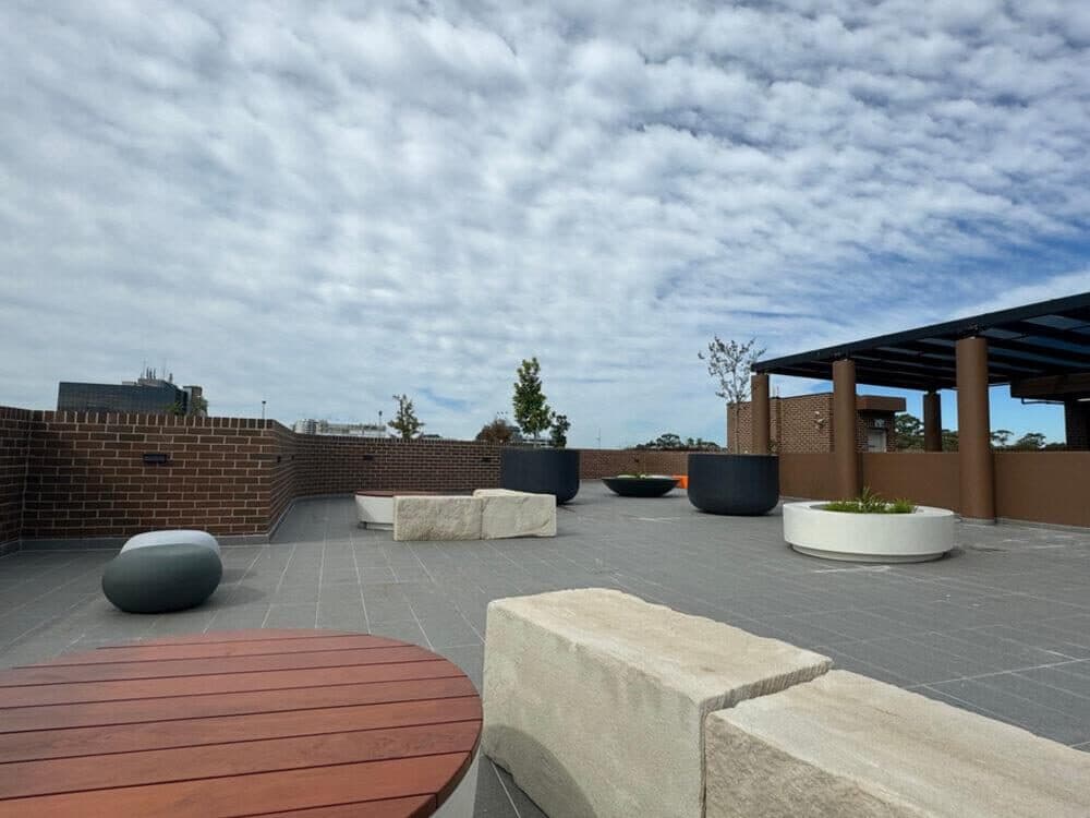 The rooftop garden at the Blacktown apartments, with stone bench seating, a timber deck, planters and a shaded pergola