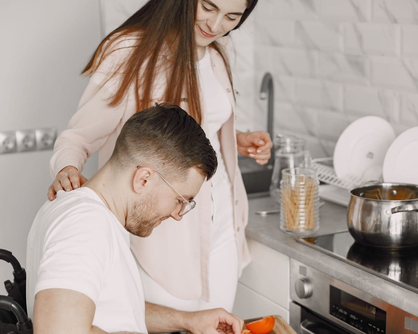 A man in a wheelchair chopping vegetables at a kitchen bench while a support worker stands beside him