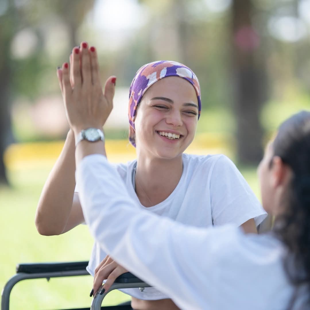 A young woman in a wheelchair sharing a joyful high five with a friend in a sunny park