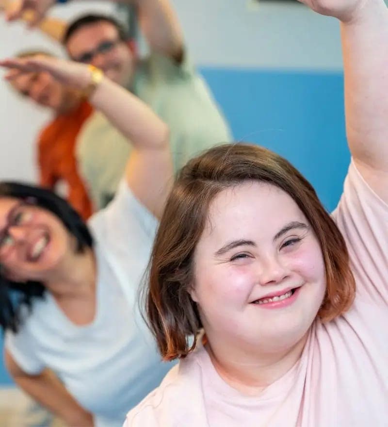 A young woman with Down syndrome smiling joyfully with her arm raised during a group activity