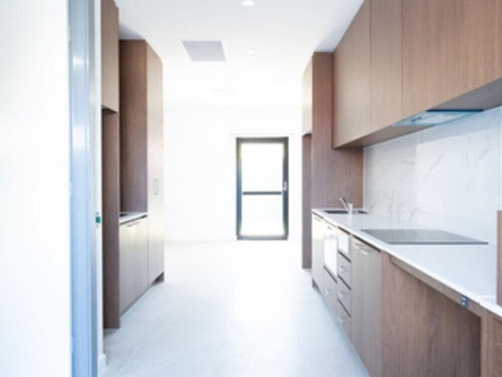 Galley kitchen in a Granville villa with timber cabinetry, a stone benchtop, induction cooktop and wide clear circulation space
