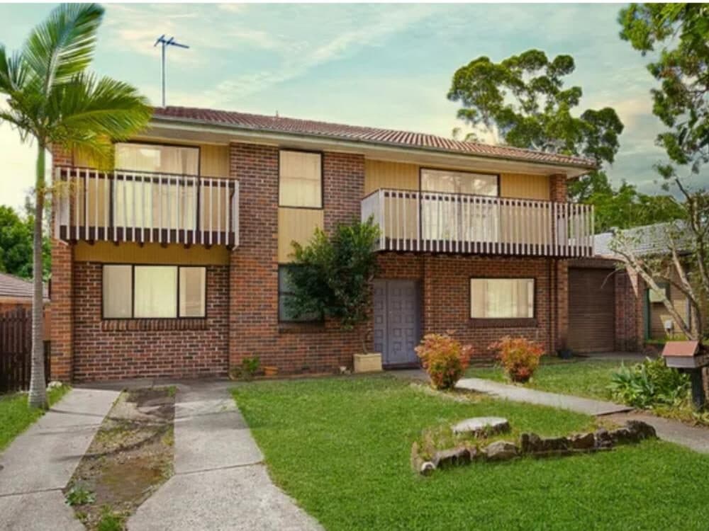 Street view of the two storey brick and weatherboard main residence at Ingleburn, with a front lawn, palm tree and upper level balcony
