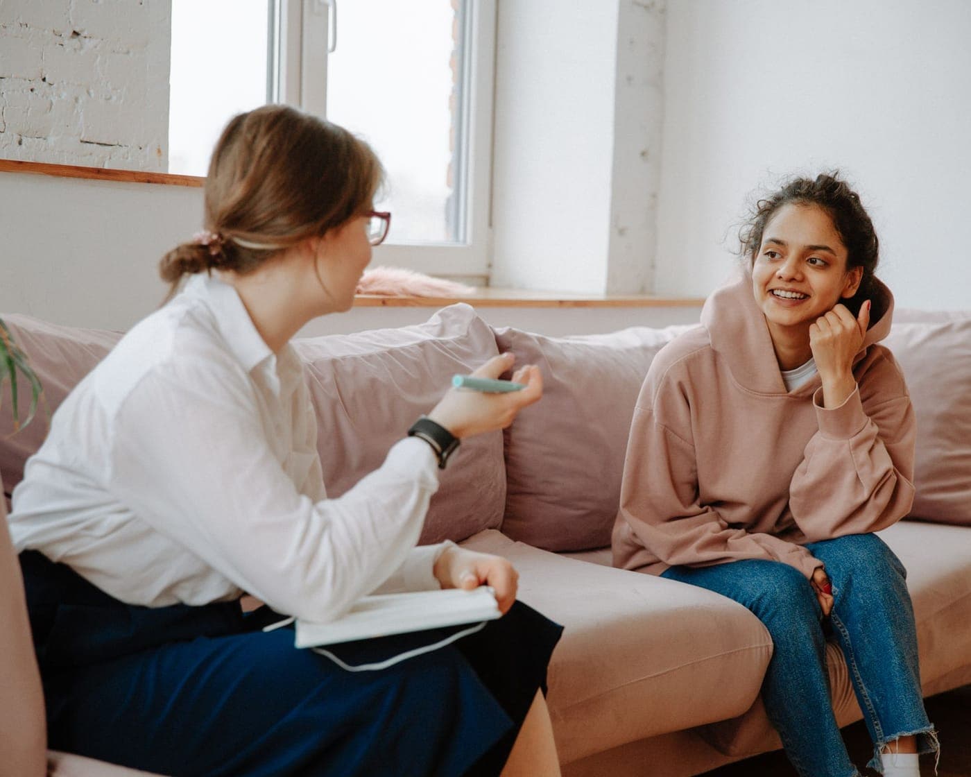 A psychologist in conversation with a smiling young woman sitting on a couch by a window