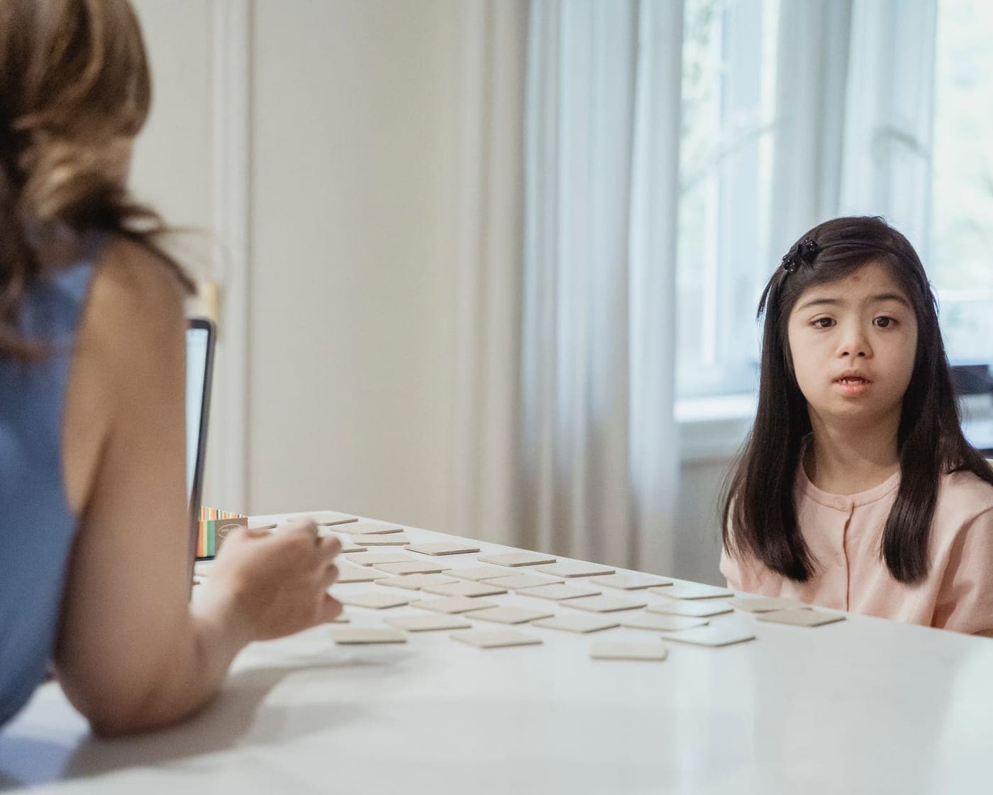 A young girl with Down syndrome sitting at a table opposite a practitioner using picture cards