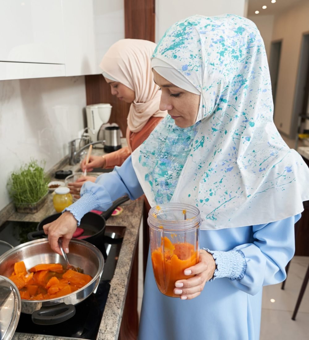 supported-independent-living-2048×2048 Muslim female friends standing at kitchen counter and cooking dinner together at home